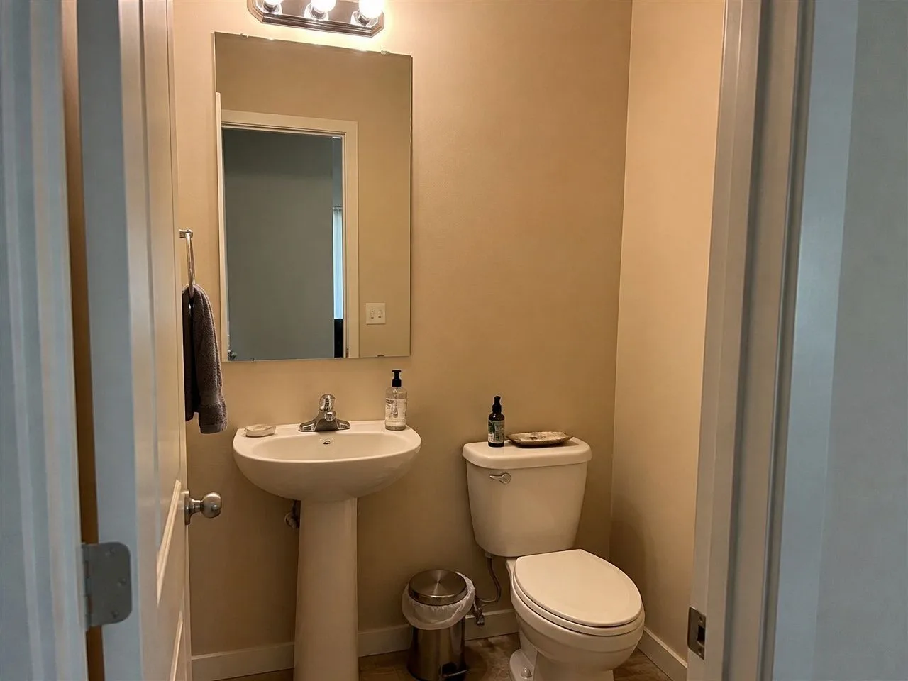A builder-basic powder room with a pedestal sink, a plain mirror and beige walls